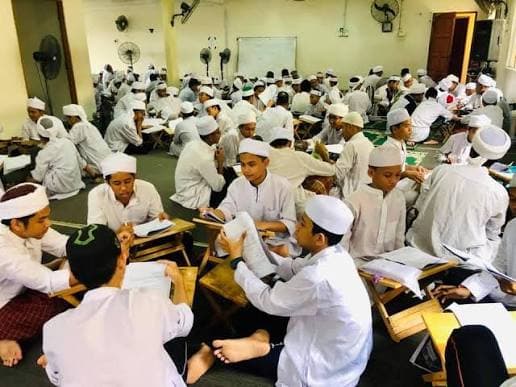 Puluhan pelajar mengulang bacaan di rehal masing-masing dalam sebuah dewan yang penuh