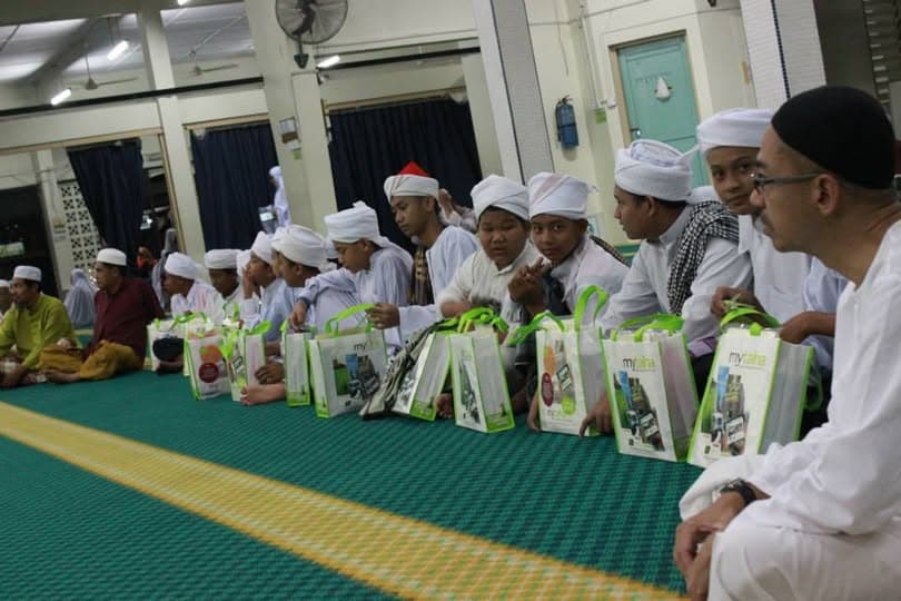 Pelajar duduk berbaris di atas permaidani surau, setiap seorang menerima bungkusan sumbangan